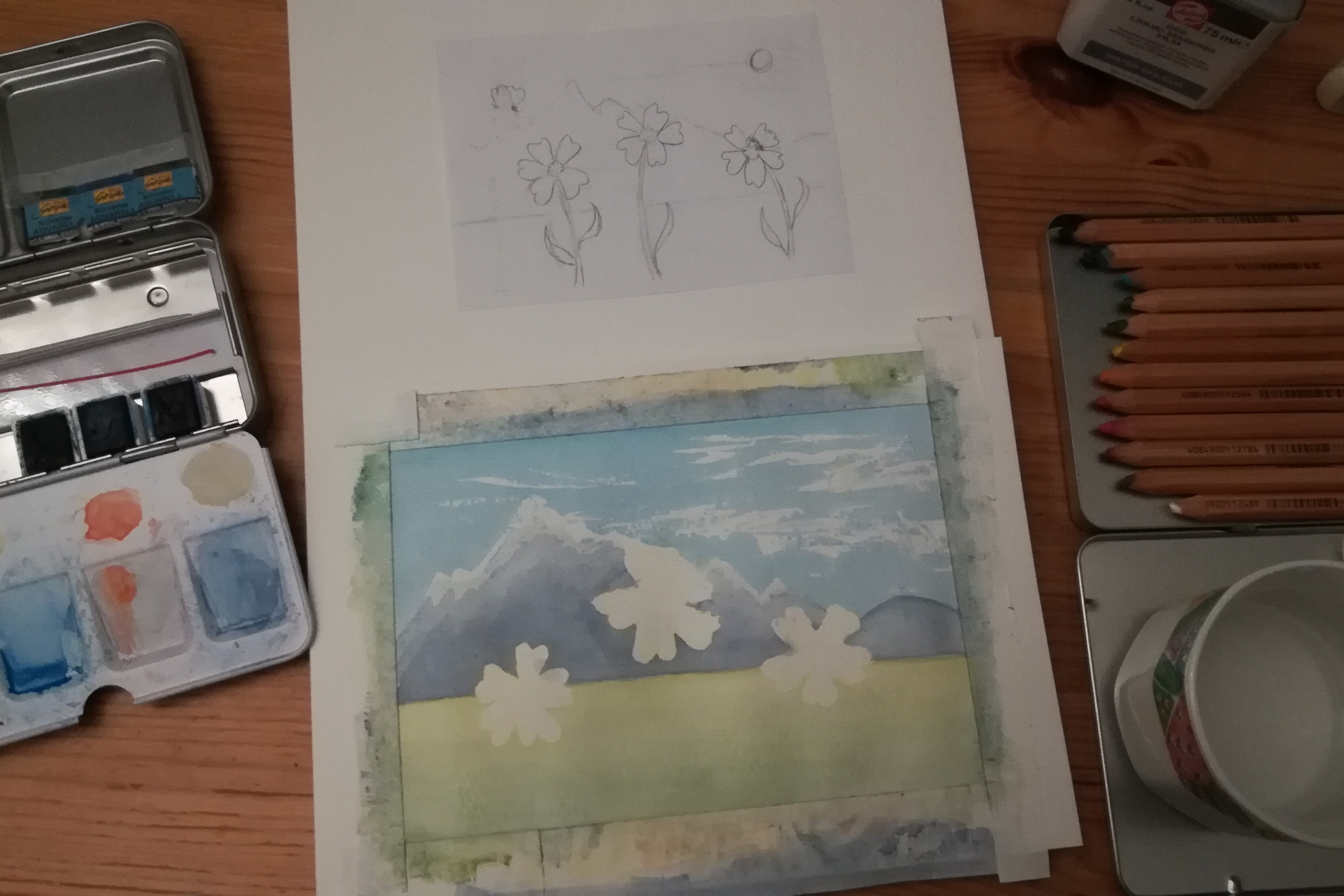 Watercolour painting in progress: flowers and mountains. Surrounded by pencil sketch, paints, and pencils. ©2022 Marie Preston