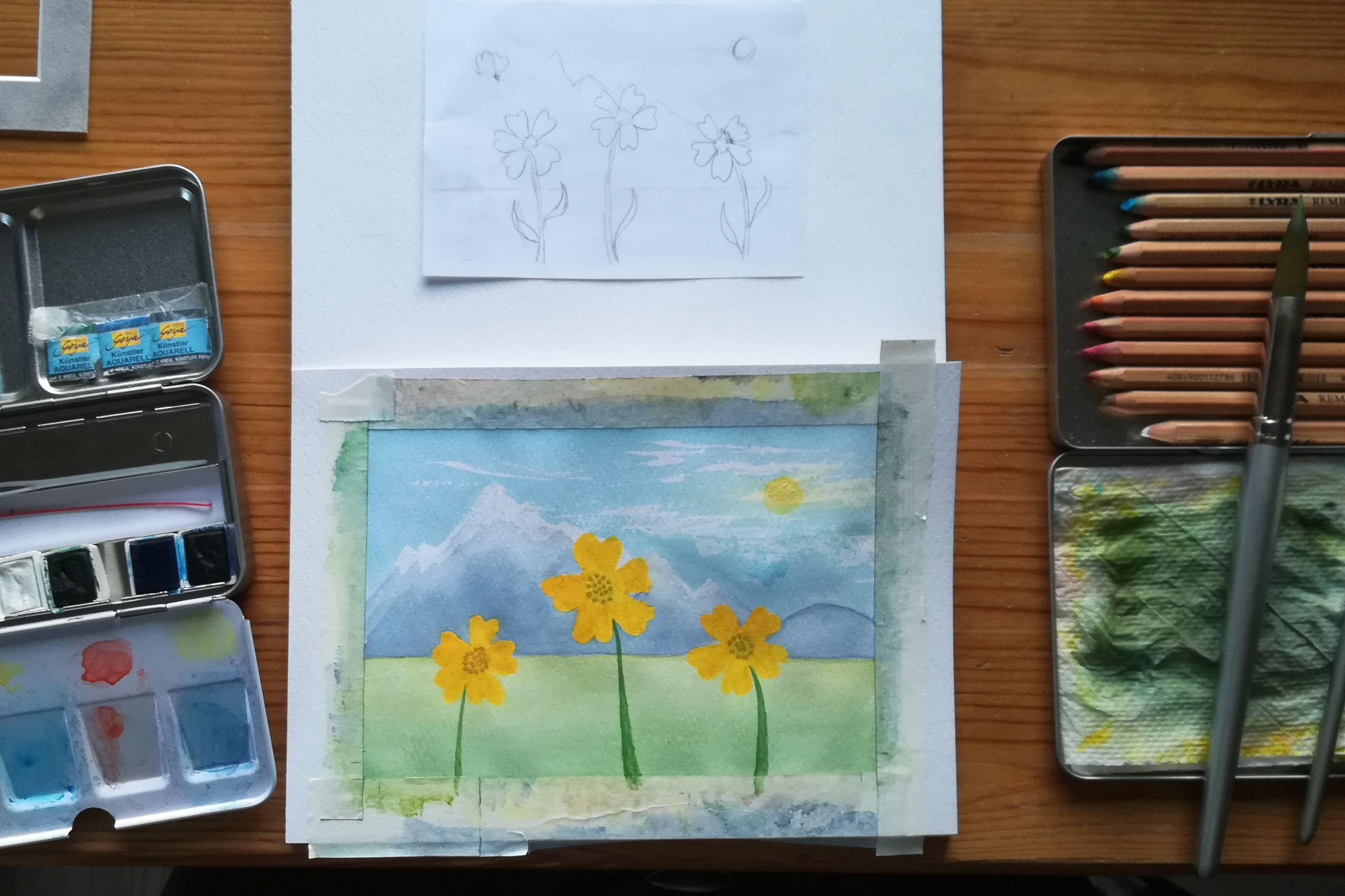 Watercolour painting in progress: flowers and mountains. Surrounded by pencil sketch, paints, and pencils. ©2022 Marie Preston