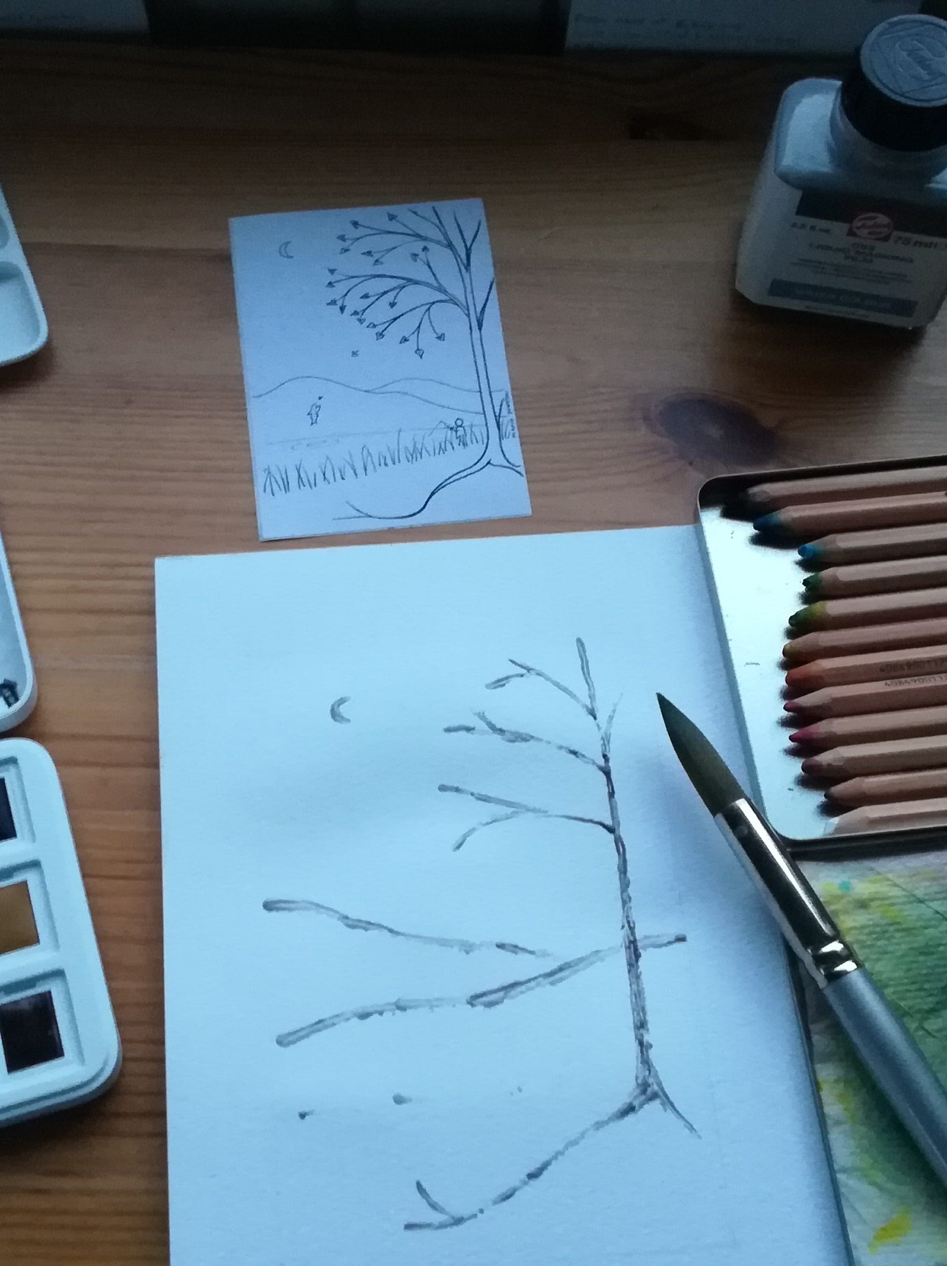 Watercolour painting in progress: tree with roots; hills; moon. Surrounded by pencils, paint, sketch